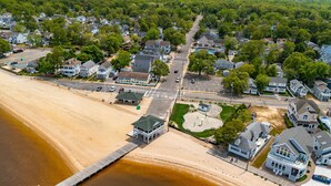 Vue aérienne d’une zone résidentielle côtière, avec des maisons, une plage et une jetée.