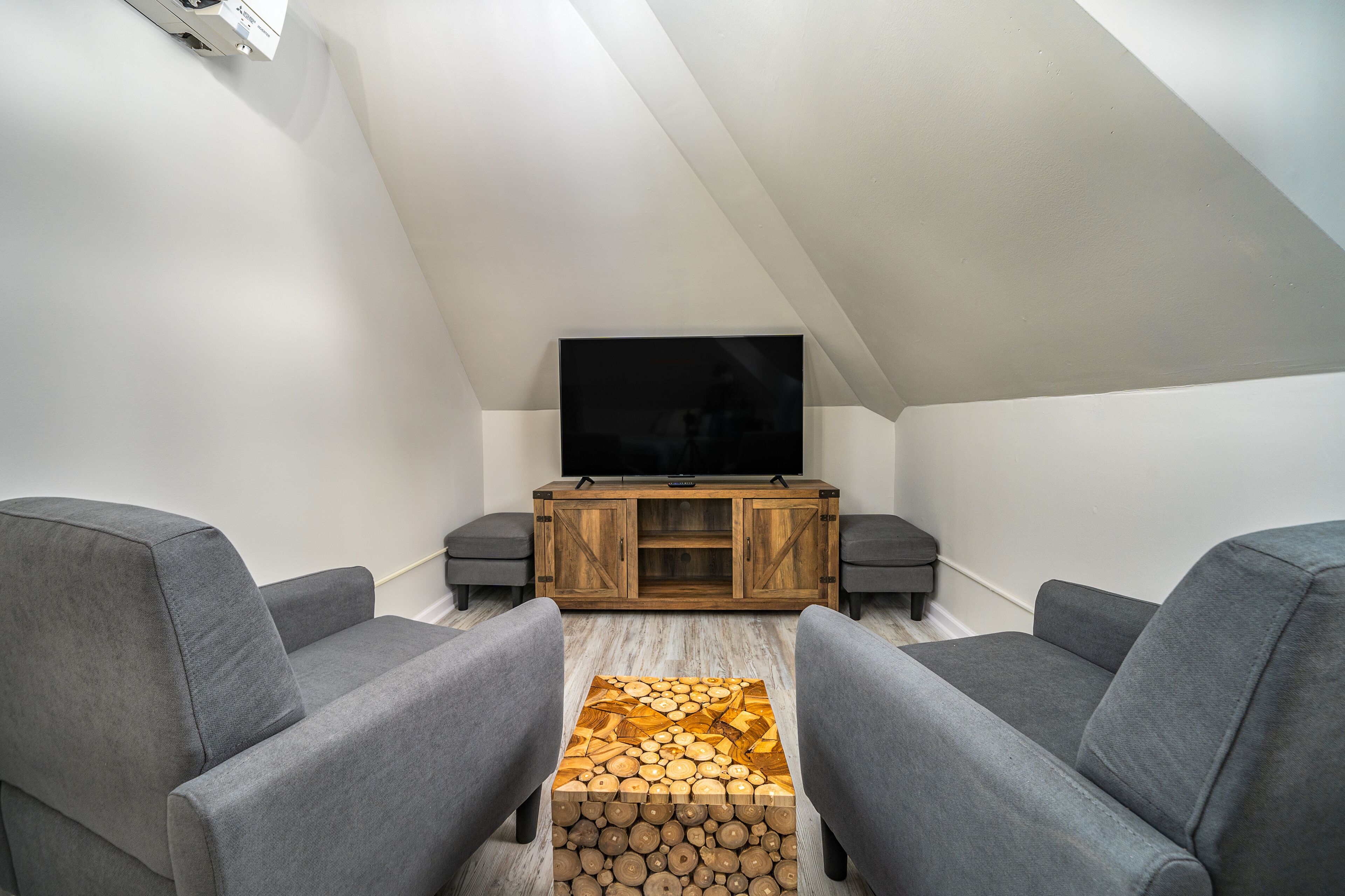 A modern loft bedroom with a sloped ceiling, a large window, a bed, and a built-in TV.