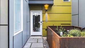 A modern building with a narrow pathway leading to a door, a planter box with plants, and a small window.