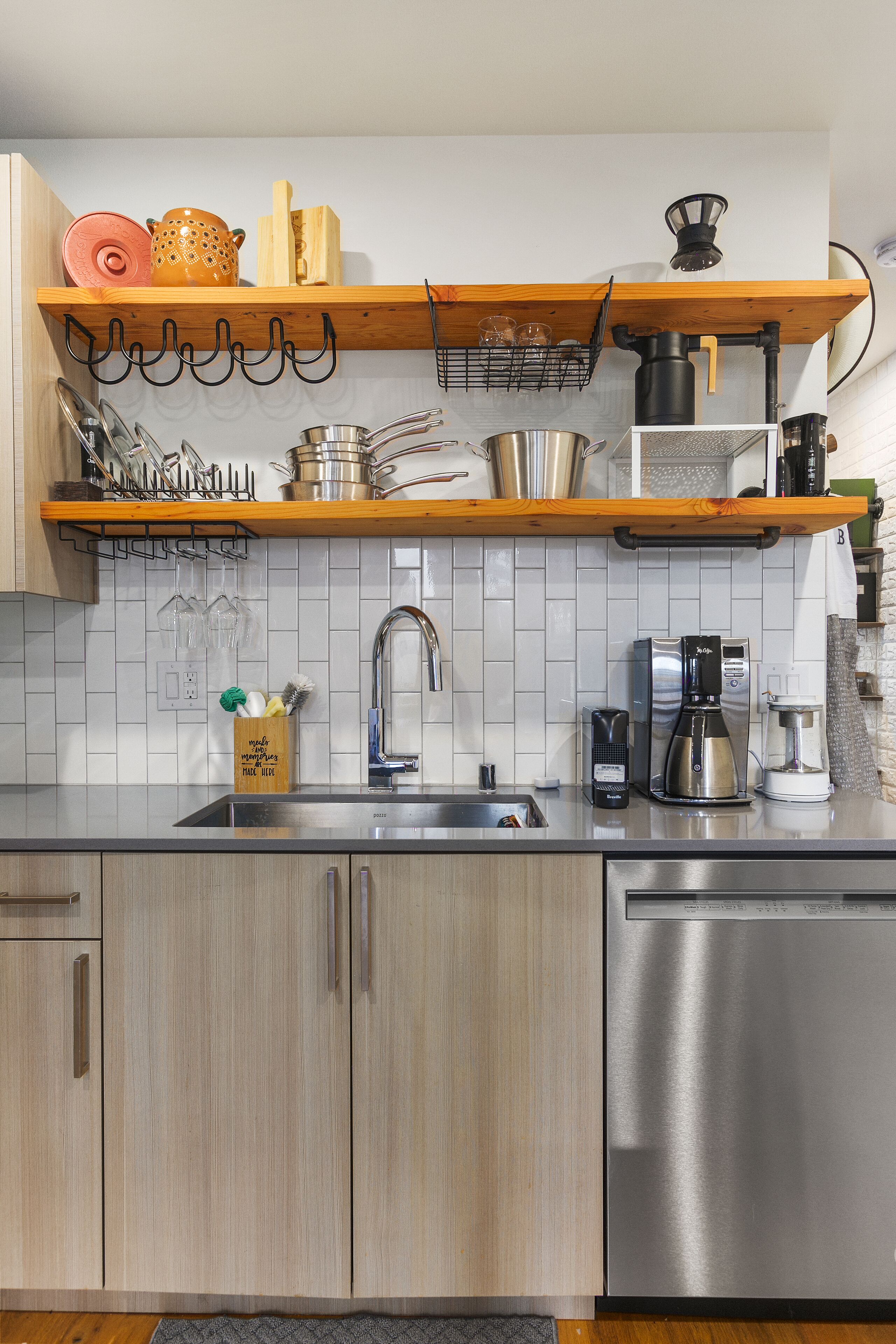 A kitchen with wooden cabinets, a stainless steel dishwasher, a coffee maker, and a hanging pot rack.