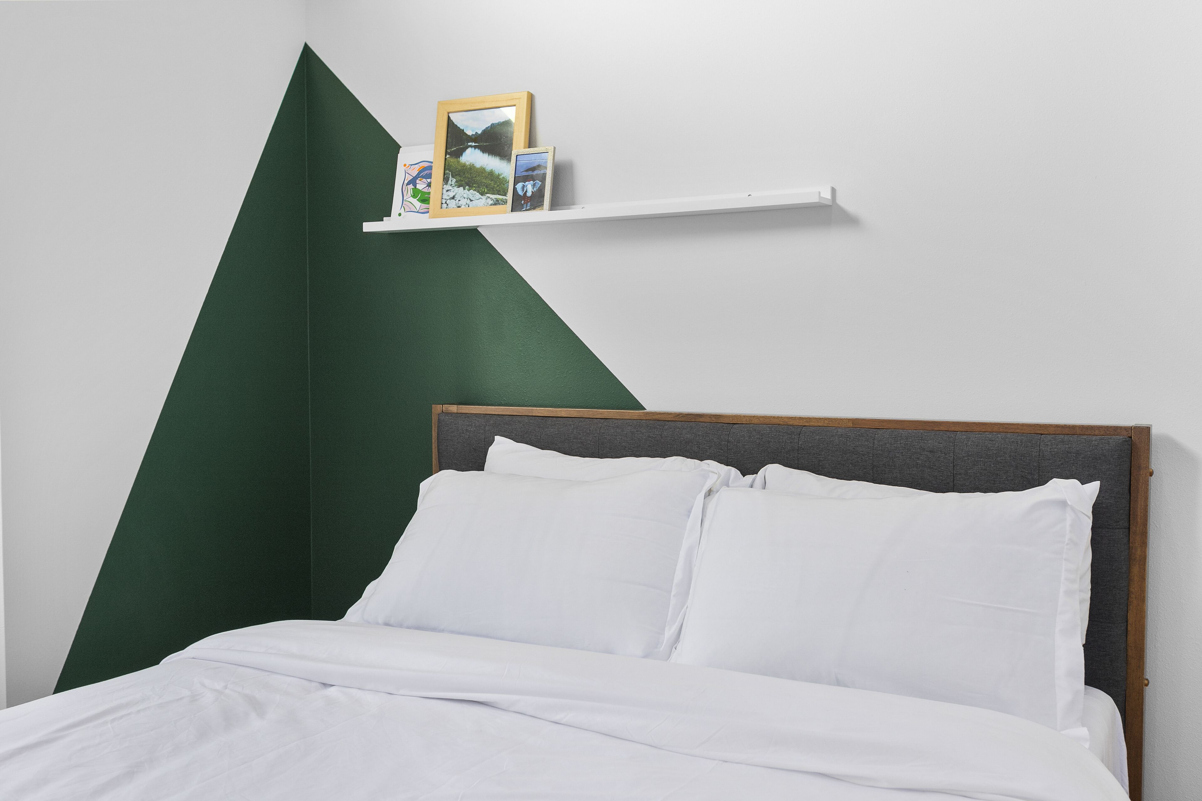 A neatly made bed with white linens, a wooden headboard, and a green accent wall.