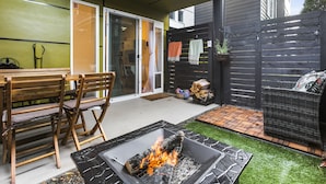 An outdoor patio with a fire pit, wooden chairs, and a black fence.
