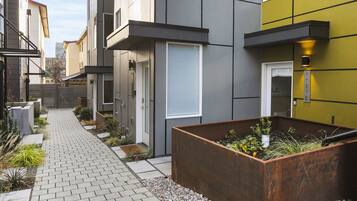 A modern residential building with a paved walkway, a planter box with plants, and a clear sky.