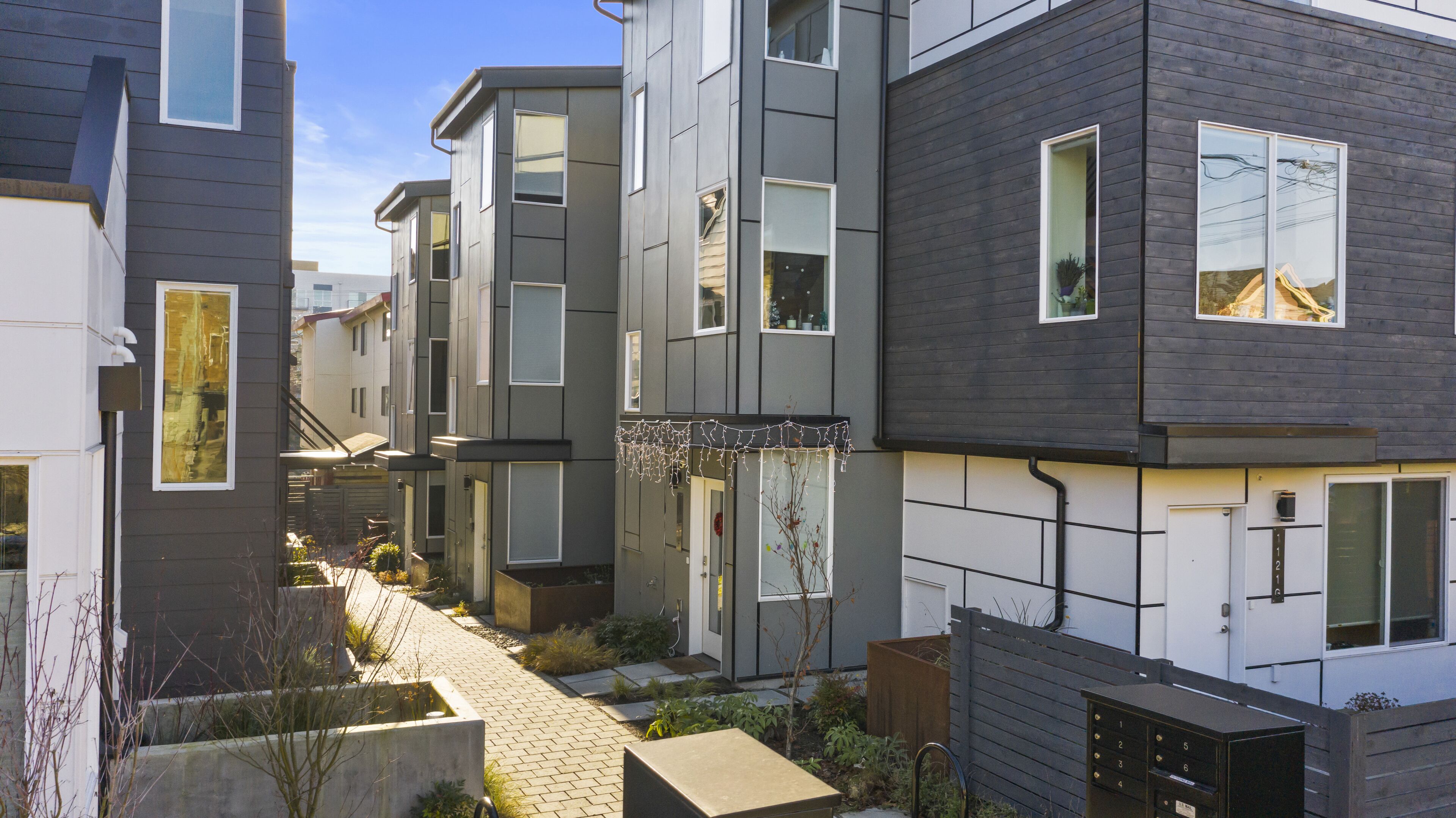 A modern multi-story residential building with a narrow pathway between the units.