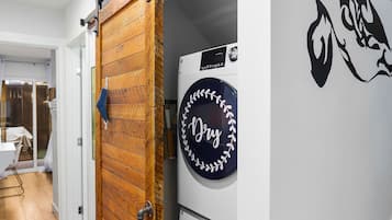 A laundry room with two washing machines, a wooden sliding door, and a wall-mounted dryer.