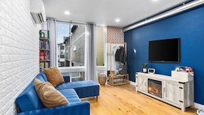 A modern living room with a blue sofa, a fireplace, a TV, and a large window.