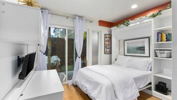 Un dormitorio moderno con cama, escritorio, estantería y puerta corrediza de vidrio que da a un espacio exterior.
