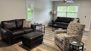 A modern living room with a leather sofa, ottoman, patterned armchair, and glass coffee table.