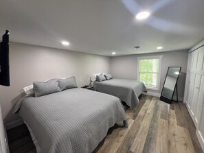 Un dormitorio con dos camas, un espejo de pie y una ventana con persianas.
