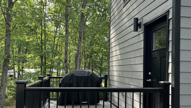 A deck with a barbecue grill, a black metal railing, and a house with grey siding and a black door.