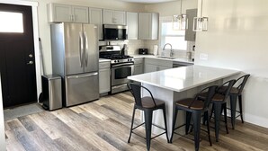 A modern kitchen with stainless steel appliances, a central island with bar stools, and a large window providing natural light.