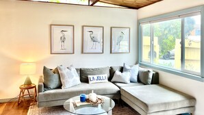 Ein modernes Wohnzimmer mit einem grauen Ecksofa, einem Glastisch und drei gerahmten Vogelbildern an der Wand.