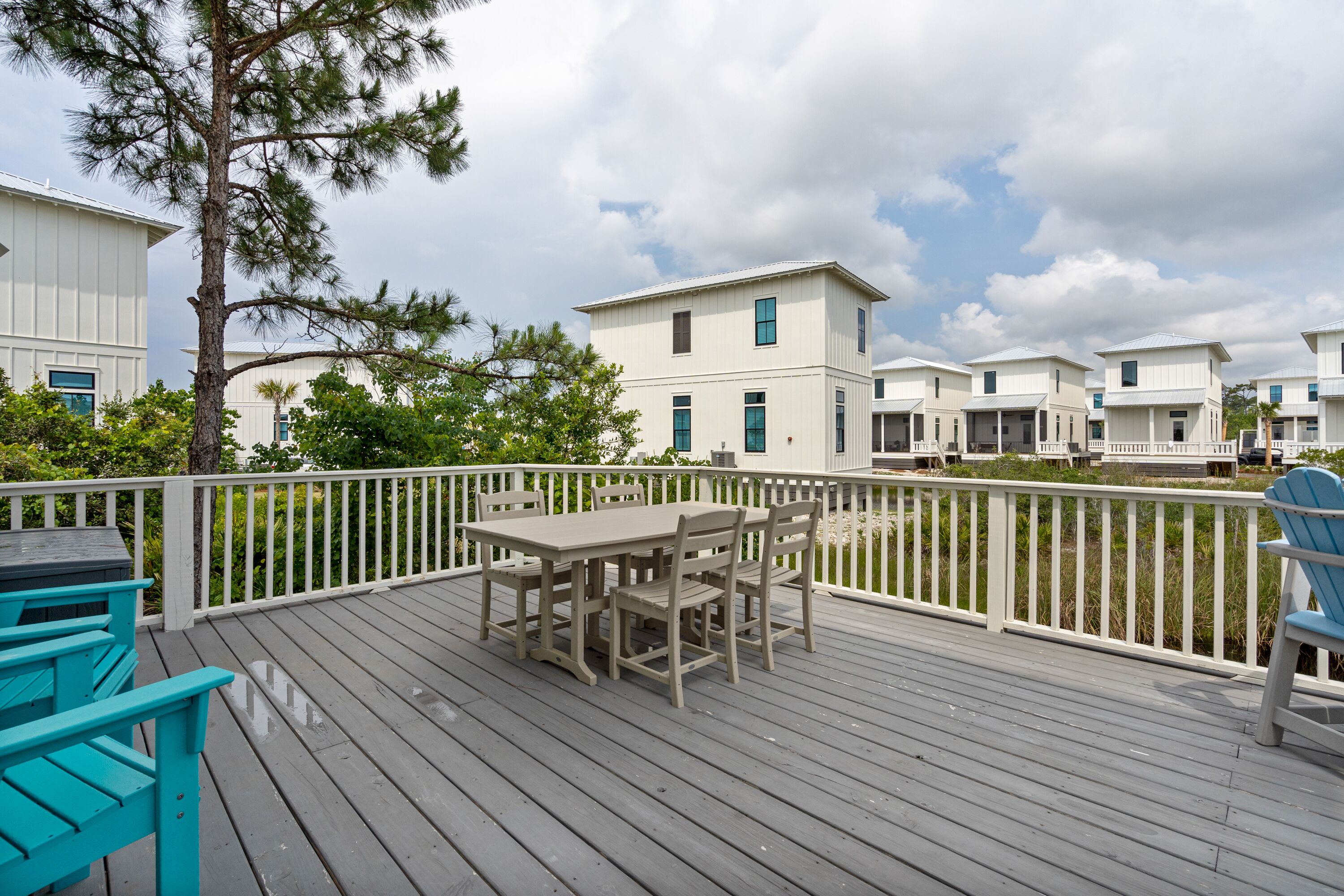 A wooden deck with a table and chairs, surrounded by a white railing, overlooking a row of white buildings.
