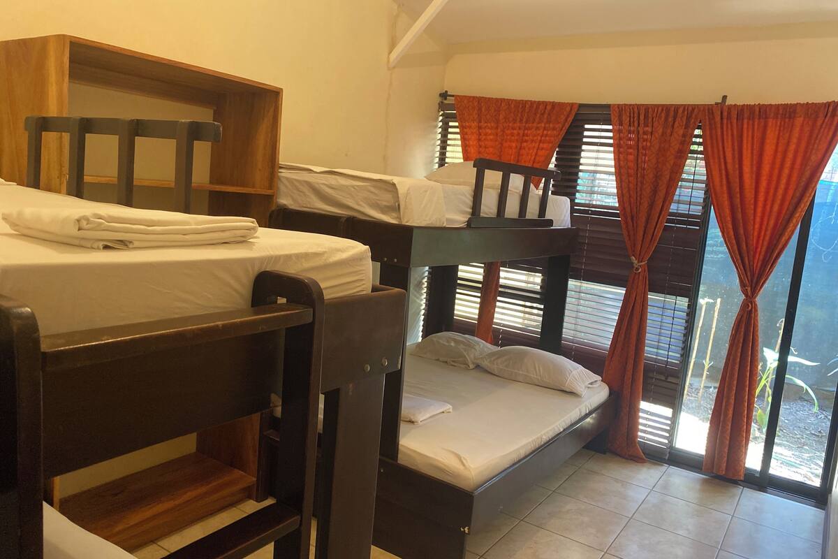 Un dormitorio con literas, un pequeño estante de madera y una ventana con cortinas.