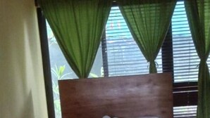 A neatly made bed with a wooden headboard, green curtains, and a window with blinds. - Cabinas Arribadas  (Cuajiniquil)