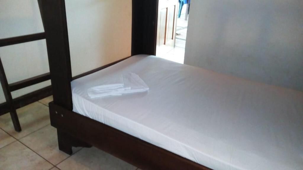 Una cama individual con colchón blanco y cabecero de madera, suelo de baldosas y pared lisa.