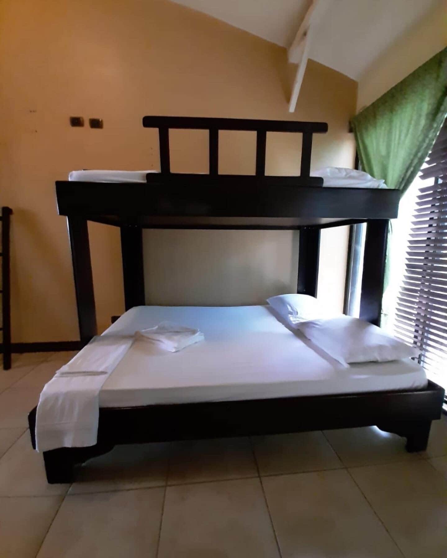 Un lit superposé avec un matelas et des oreillers, une table de chevet et une fenêtre avec des stores.