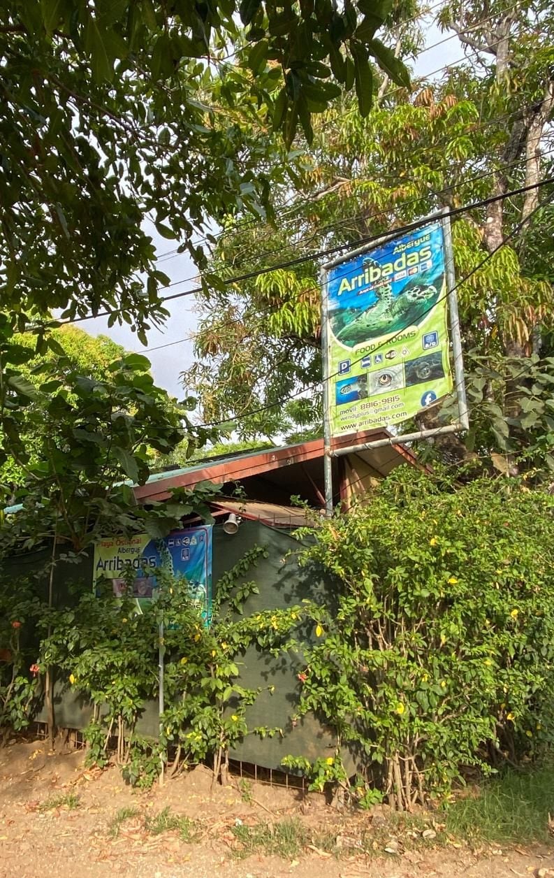 Un edificio con fachada verde y un cartel publicitando comida y habitaciones.