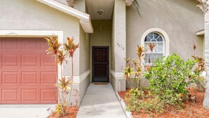 A residential house with a red garage door, a front door, and a small garden with plants. - Quiet Getaway to Tampa & Orlando (Mulberry)