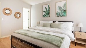 A bedroom with a bed, two wall-mounted mirrors, and two framed tropical plant prints. - Quiet Getaway to Tampa & Orlando (Mulberry)