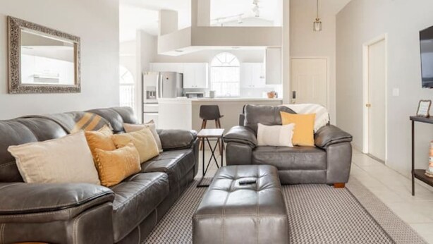 A modern living room with a grey leather sectional sofa, a small coffee table, and a patterned rug. - Quiet Getaway to Tampa & Orlando (Mulberry)