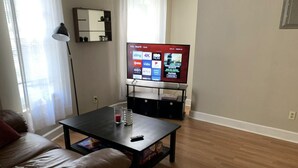 Ein Wohnzimmer mit Fernseher auf einem Schrank, einem Couchtisch mit Fernbedienung und einem Glas sowie einer Couch.