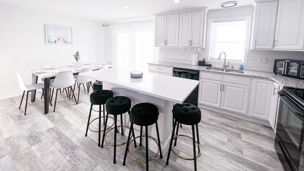 Una cocina moderna con armarios blancos, una isla grande, taburetes de bar y una zona de comedor con sillas.