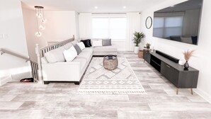 Una sala de estar moderna con un sofá modular, un televisor de pantalla plana y una escalera.
