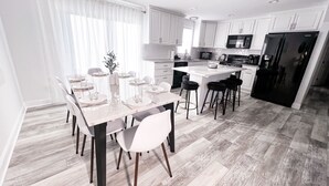 Una cocina moderna con armarios blancos, una isla central y un comedor con una mesa y sillas blancas.