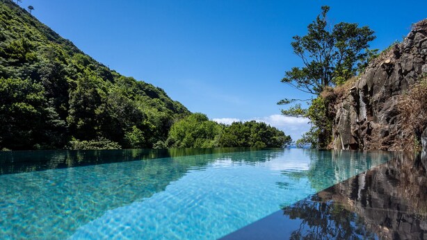 Une piscine d’eau cristalline, d’un bleu éclatant, offrant une vue sur une végétation luxuriante et un paysage rocheux.