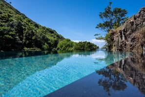 Ein klares, blaues Schwimmbecken mit Blick auf üppige Vegetation und felsiges Gelände.