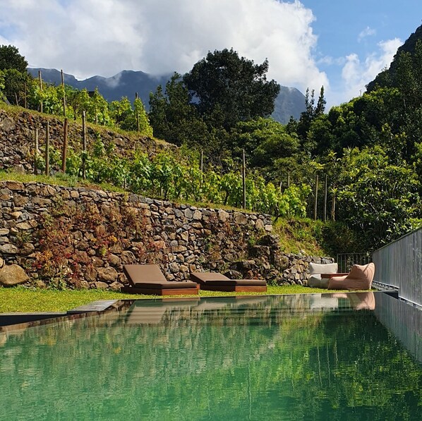Ein Pool mit Liegestühlen, einer Steinmauer und einer Bergkulisse im Hintergrund.