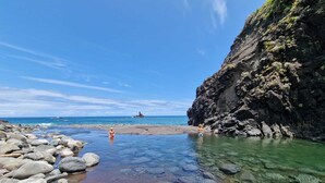 Une plage rocheuse aux eaux cristallines, une formation rocheuse visible au loin et une falaise abrupte.