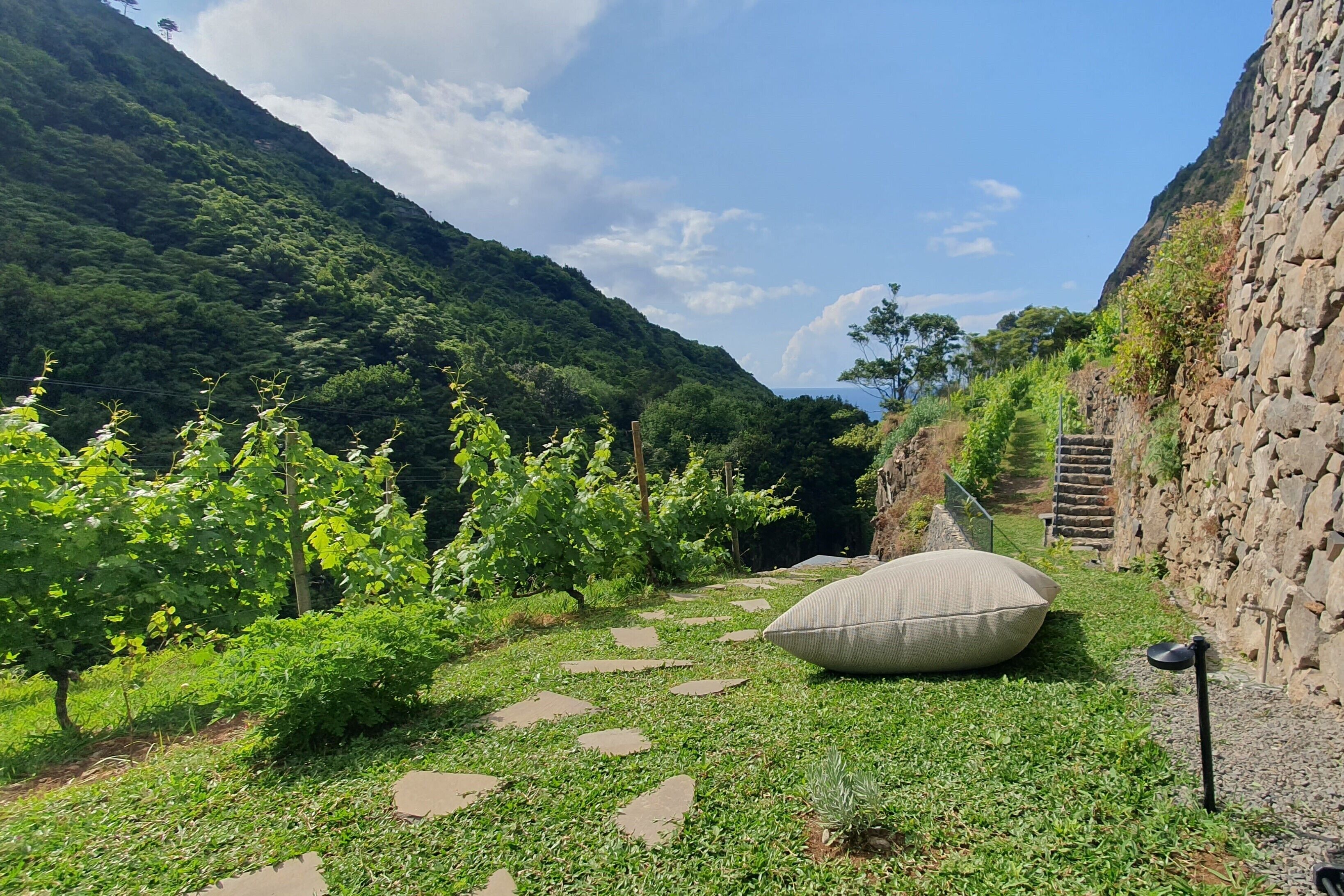 A garden with stepping stones, a large cushion, and a stone wall.