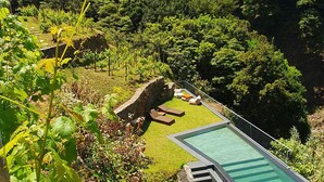 Un espace piscine avec des marches menant à une terrasse enherbée, entouré d’une végétation luxuriante et dominé par un paysage montagneux.