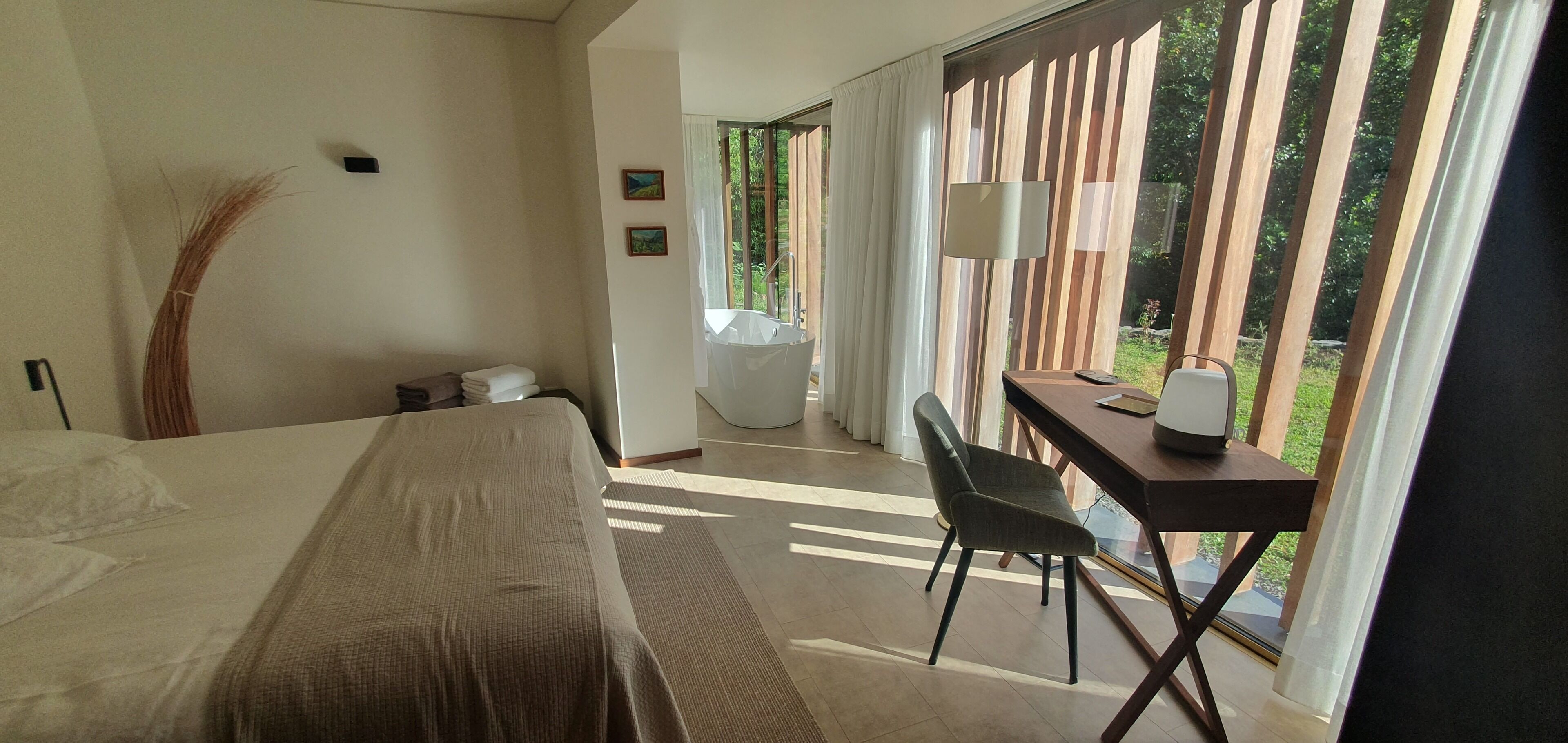 Habitación de hotel con cama, escritorio con silla, lámpara y vistas al exterior.