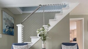 En trappa med modern design, två blå fåtöljer med mönstrade kuddar, ett litet bord med en vas med blommor och en tavla på väggen.