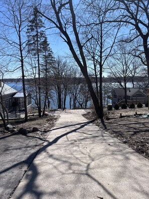 Un chemin pavé mène à un quartier résidentiel, avec des maisons et une étendue d’eau en arrière-plan.
