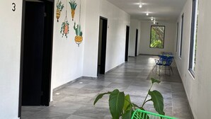 A hallway with a tiled floor, a green chair with a laptop, and a table with chairs in the distance.