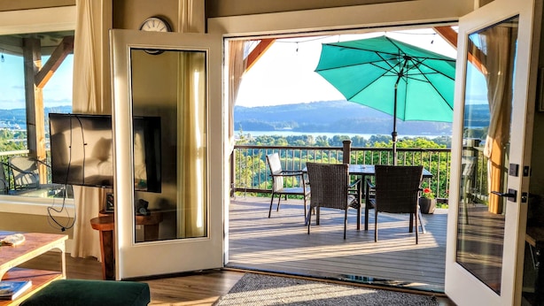 Un salon avec un téléviseur, une table basse et un canapé. Une porte-fenêtre coulissante donne sur une terrasse extérieure équipée d’une table, de chaises et d’un grand parasol.