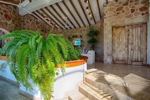 Un hall aux murs en pierre, doté d’un plafond en bois, d’un comptoir d’accueil blanc et d’une grande porte en bois.