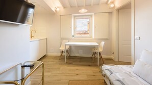 Une petite pièce comprenant un lit, un bureau avec deux chaises, un téléviseur fixé au mur et une fenêtre.