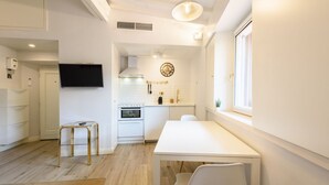 Une cuisine moderne avec des meubles blancs, un four encastré et un coin repas comprenant une table et des chaises blanches.