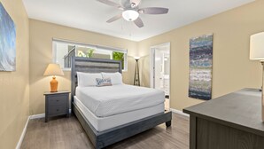 Un dormitorio con cama, mesita de noche, lámpara, ventilador de techo y una obra de arte.