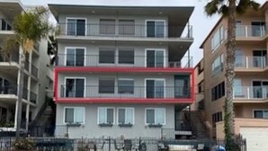 Un edificio residencial de varios pisos con balcones, una sección central de marco rojo y una palmera en primer plano.