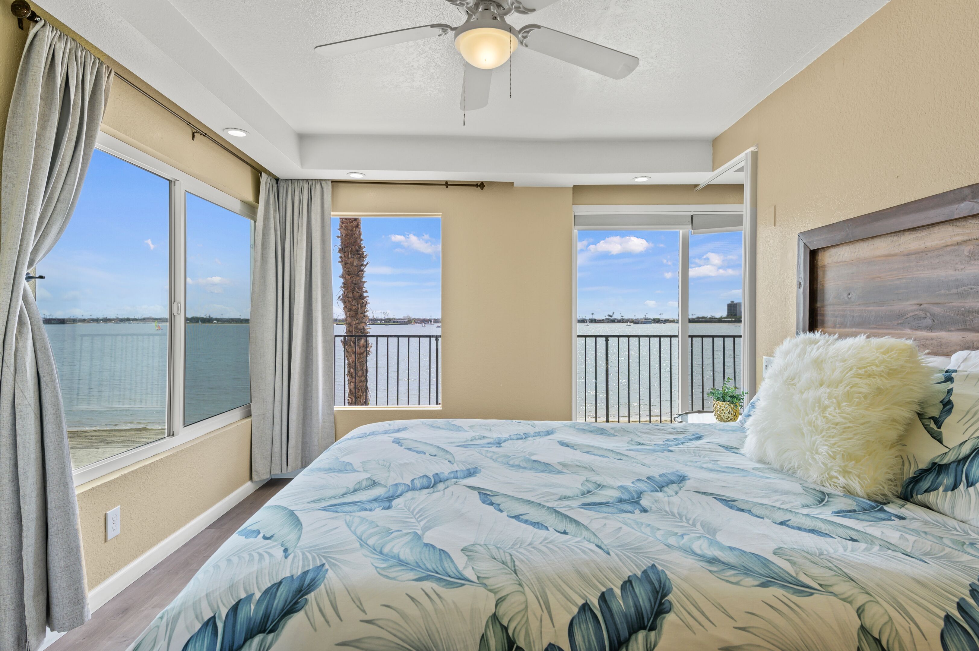 A bedroom with a large bed, a ceiling fan, and a view of the ocean through large windows.