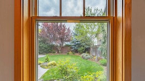 Une fenêtre donnant sur un jardin bien entretenu, une clôture en bois et une maison en arrière-plan.