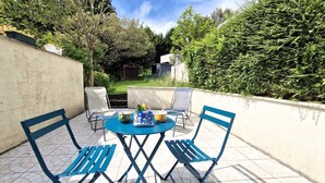 An outdoor patio with a round table and blue chairs, surrounded by a low wall and dense greenery. - Meschers sur Gironde - TOP HOLIDAY VILLA - IDEAL FAMILY RESIDENCE (MESCHERS SUR GIRONDE)