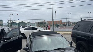 Ein Parkplatz mit mehreren Autos und einem Sportplatz im Hintergrund.