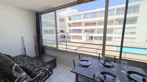 A balcony with a dining table set for four, a sofa, and a view of a modern building and swimming pool.